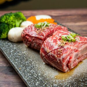 Mouthwatering marbled beef and fresh vegetables artfully presented on a stone plate.