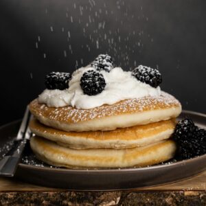 Mouthwatering pancakes topped with cream and blackberries, dusted with powdered sugar.